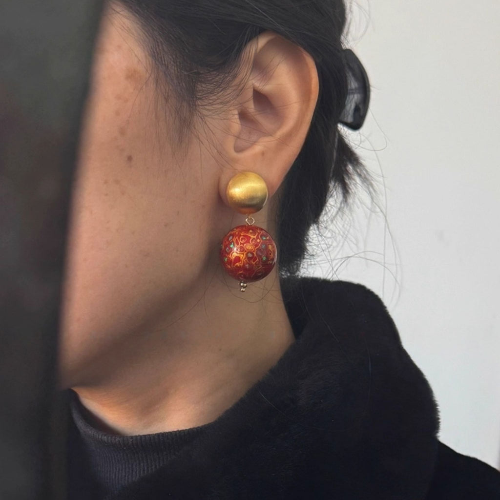 Close-up of a person wearing a gold and red earring against a neutral background