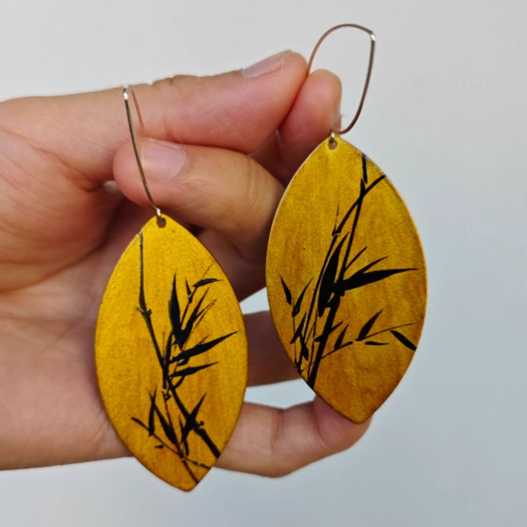 Hand holding yellow earrings with black bamboo design against a light  LacLume Hand-Painted Lacquer Jewelry Golden Autumn Bamboo Shadow for Fall Outfits 
background