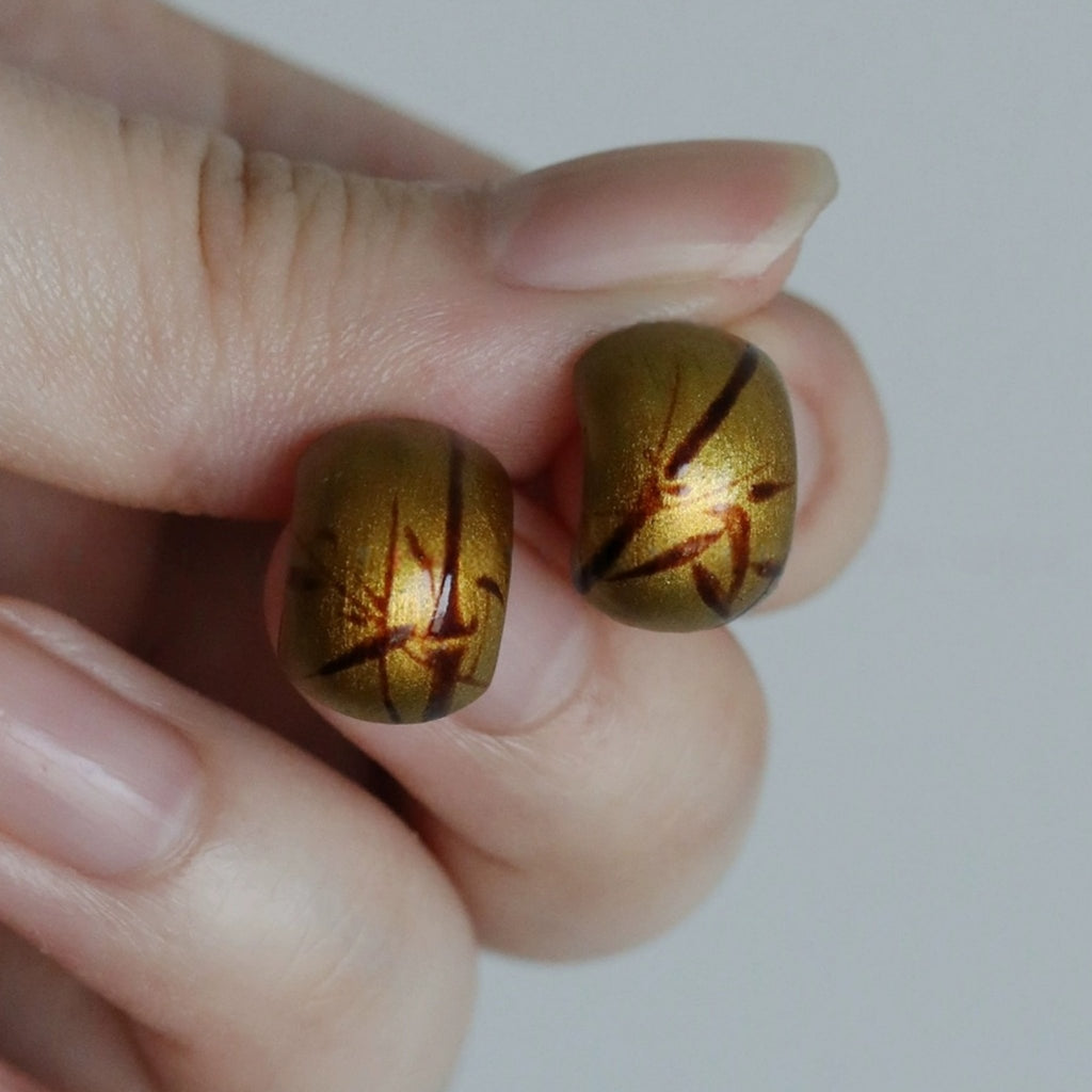 Gold earrings with a star pattern held between fingers against a white background