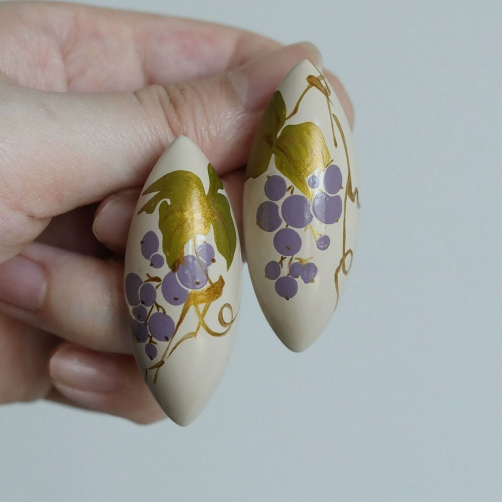 Two decorative earrings with grape designs held between fingers against a light background LacLume Handcrafted Lacquer Earrings Purple Berry Bubbles Niche Daily Style