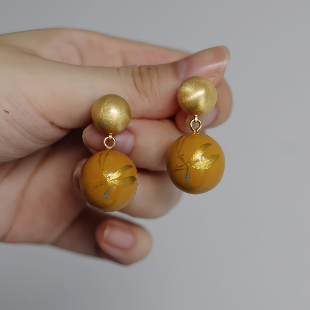 Gold and yellow earrings held between fingers against a neutral background LacLume Summer Firefly Handmade Lacquer Jewelegant Temperament Earringselry