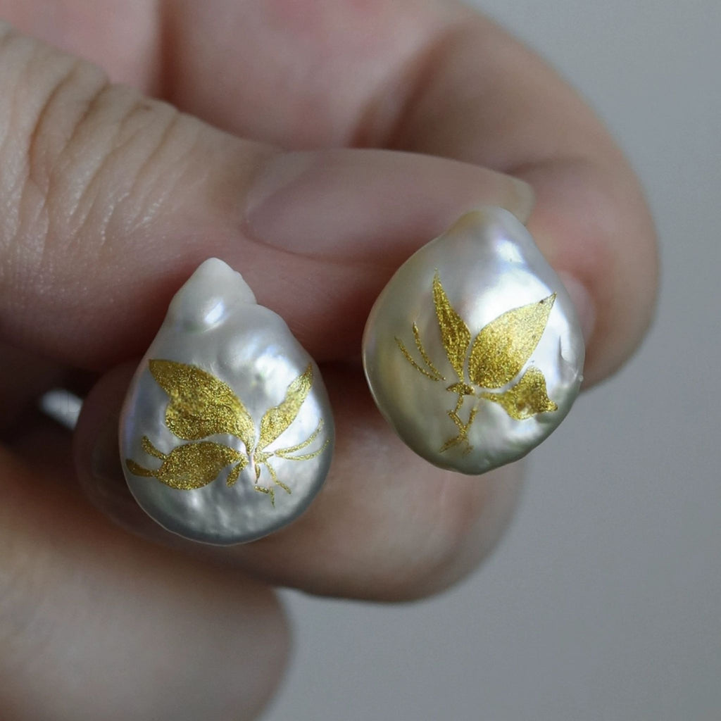 Pearl earrings with gold leaf design held between fingers against a neutral background LacLume Hand-Painted Lacquer Earrings Baroque Pearl Gilded Butterfly