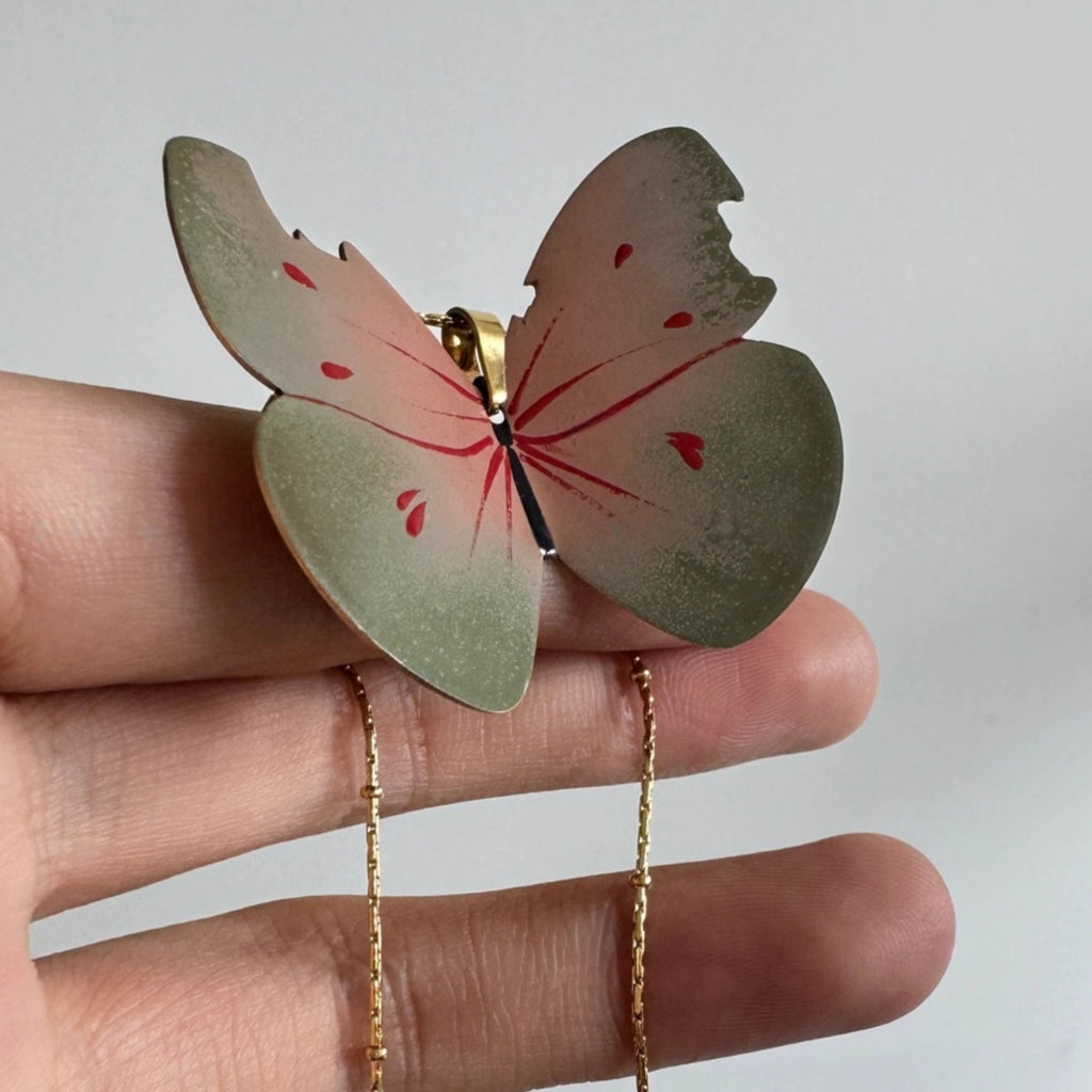 Butterfly-shaped pendant on a chain held in a hand against a plain background