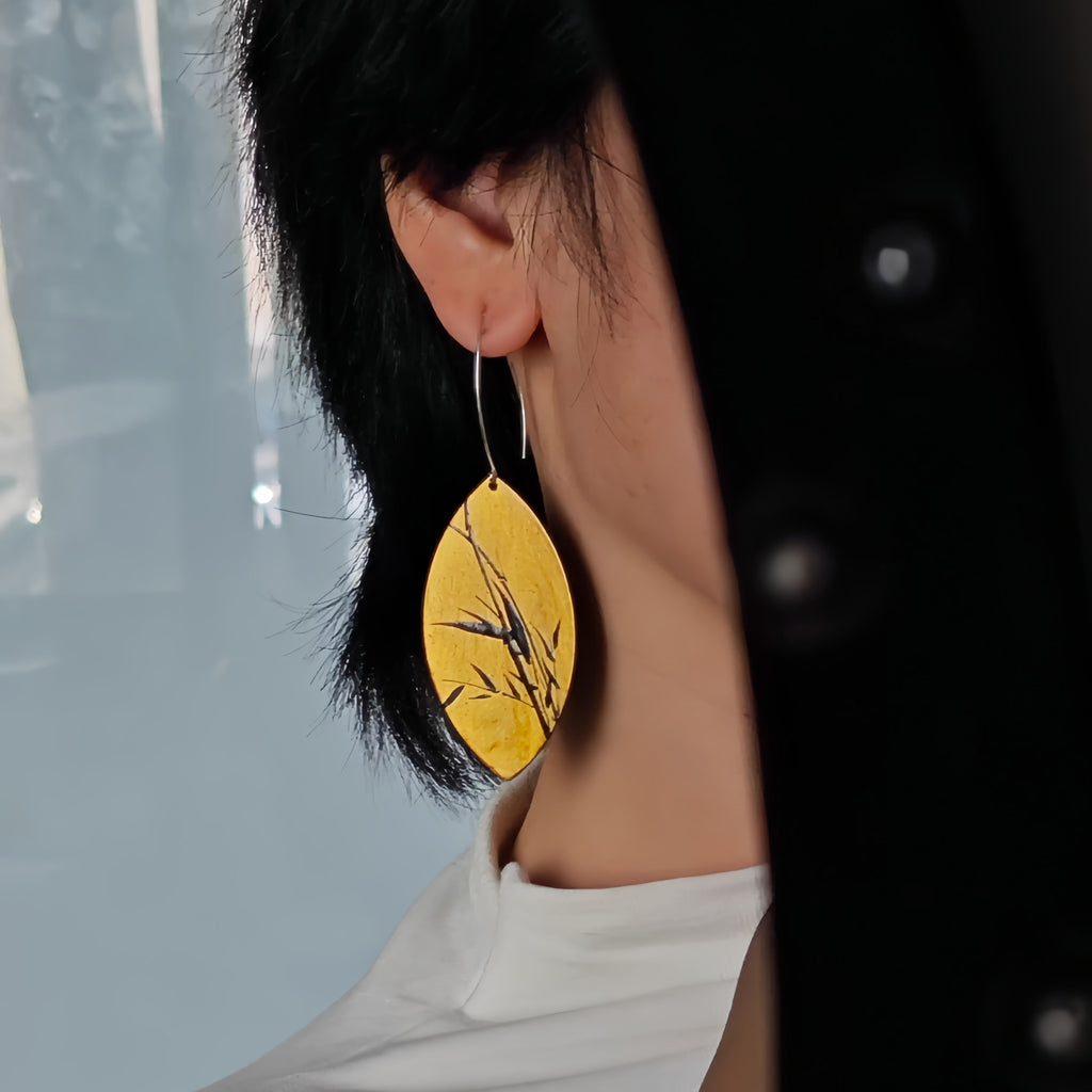 Person wearing a yellow earring with a nature design, blurred background LacLume Hand-Painted Lacquer Jewelry Golden Autumn Bamboo Shadow for Fall Outfits