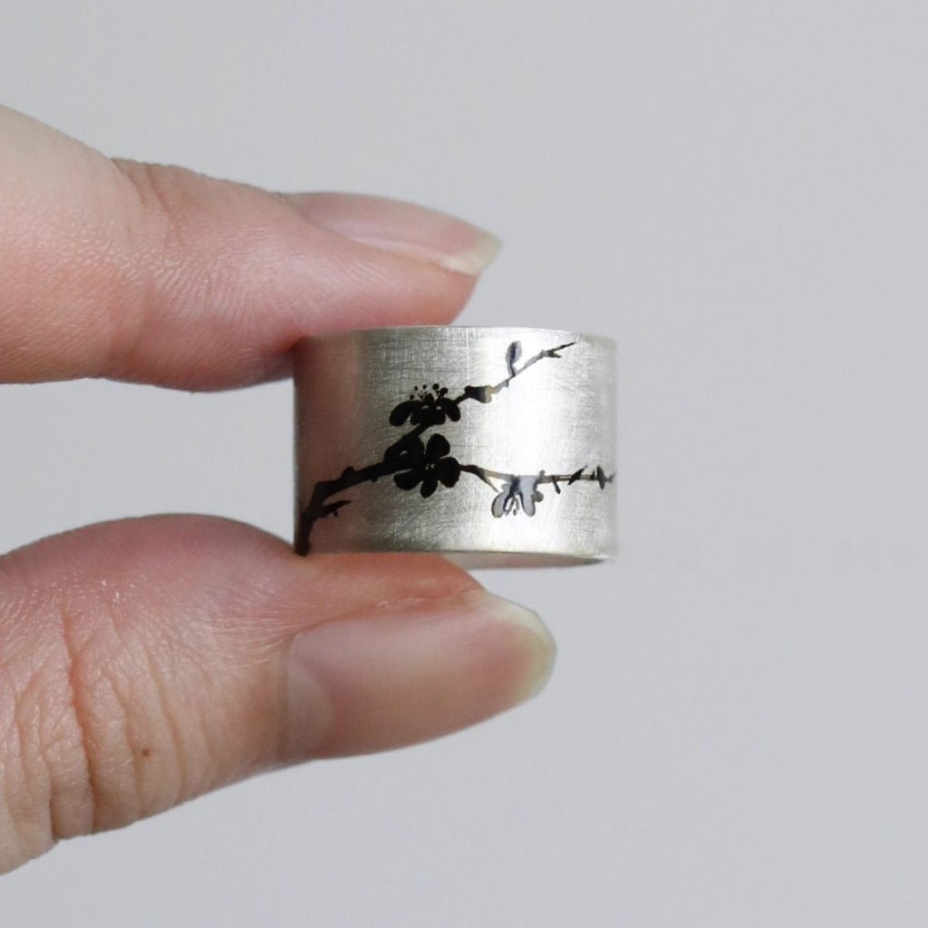 Silver ring with black floral design held between fingers against a plain background