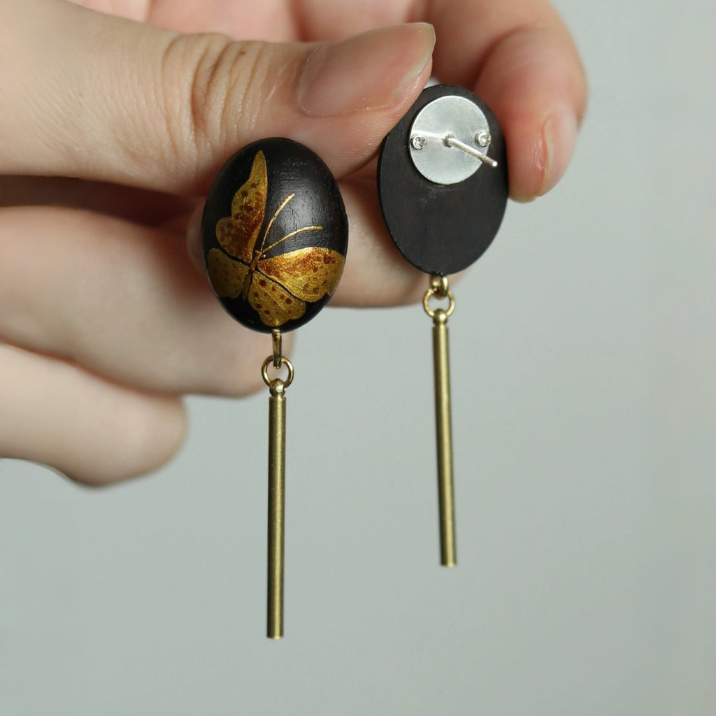 Black earrings with gold butterfly design held by a hand against a neutral background LacLume Hand-Painted Lacquer Earrings Gold Butterfly Glamour Understated Elegance