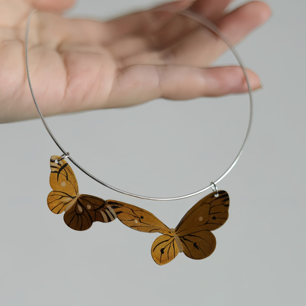 Butterfly-shaped pendant on a chain held by a hand against a neutral background