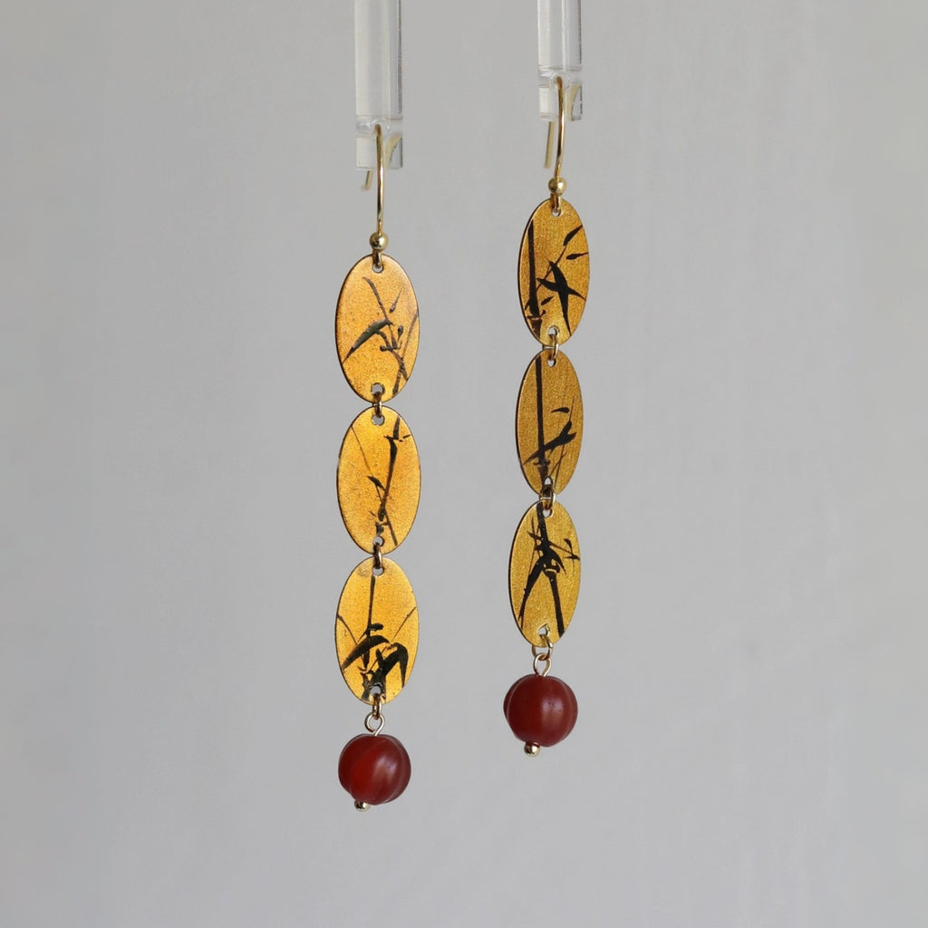 Pair of earrings with yellow oval stones and red beads on a gray background