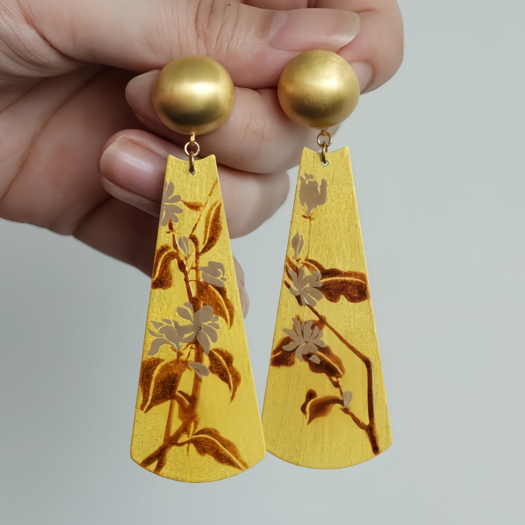 Gold earrings with floral patterns held by a hand against a neutral background LacLume Earrings Summer Jasmine Plant Pattern Jewelry Handmade Lacquer Jewelry