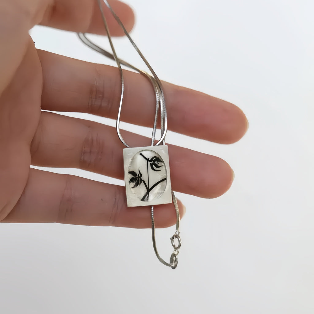 Silver necklace with a square pendant featuring a floral design held in a hand against a white background LacLume Starry Sky Cosmos Flower Necklace Hand-Painted Lacquer Dreamy Vibe
