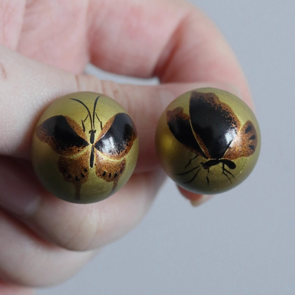 Two round objects with butterfly designs held between fingers against a neutral background