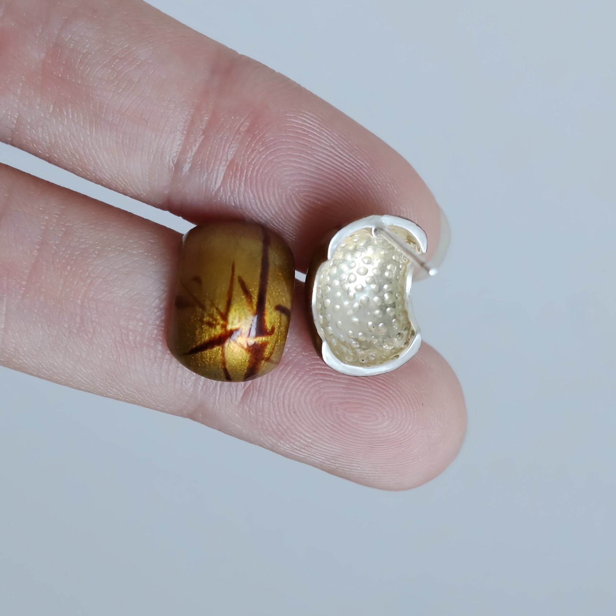 Close-up of a hand holding two small decorative items, one brown and one gold, against a plain background.