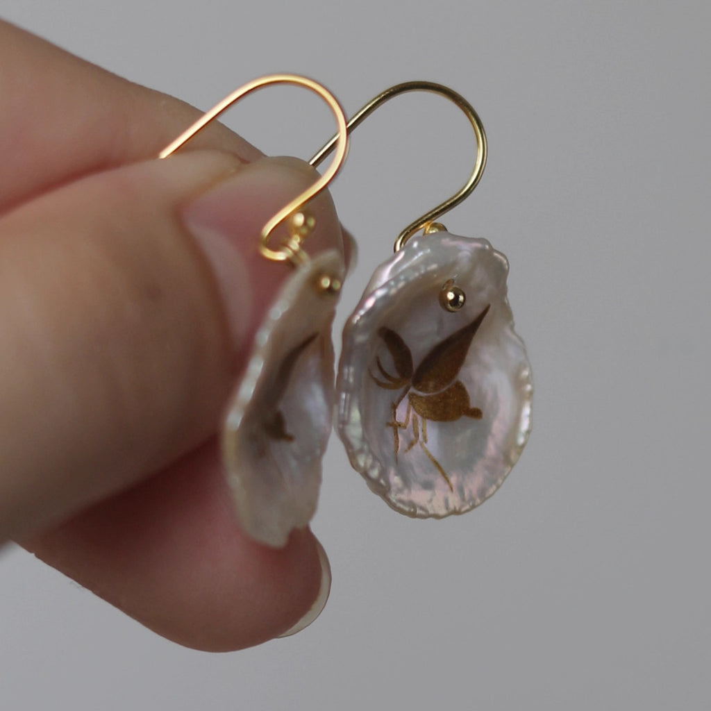 Shell earrings with gold hooks held by a hand against a neutral background LacLume Handcrafted Golden Lacque Butterfly Lacquer Earrings Shell