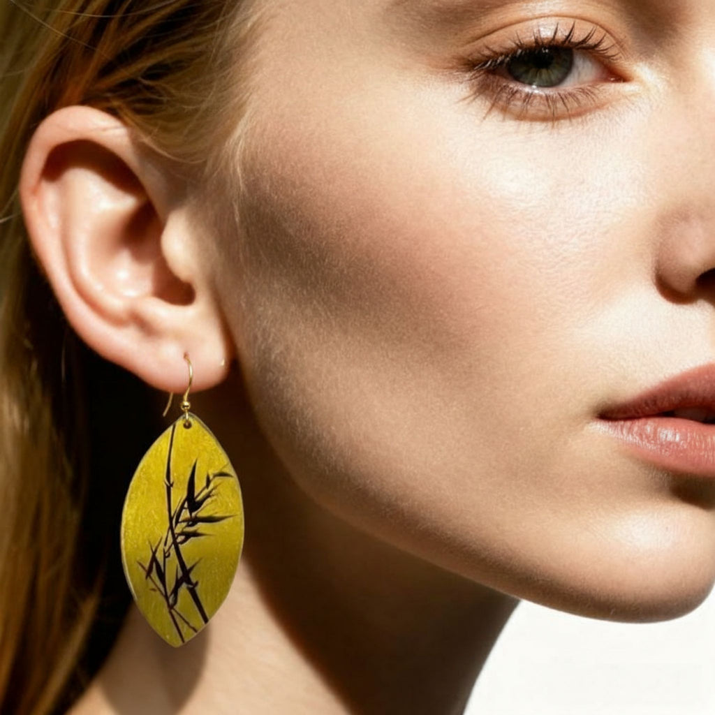 Close-up of a woman wearing a yellow earring with black leaf design. LacLume Hand-Painted Lacquer Jewelry Golden Autumn Bamboo Shadow for Fall Outfits