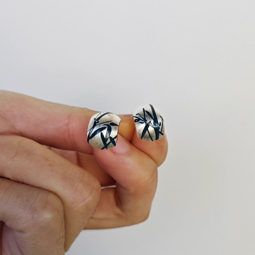 Silver earrings with black and white design held between fingers against a plain background
