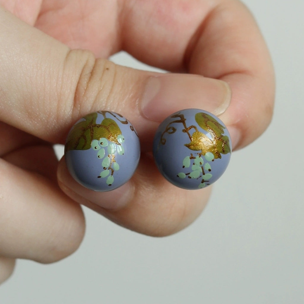 Two small round objects with floral design held between fingers against a neutral background