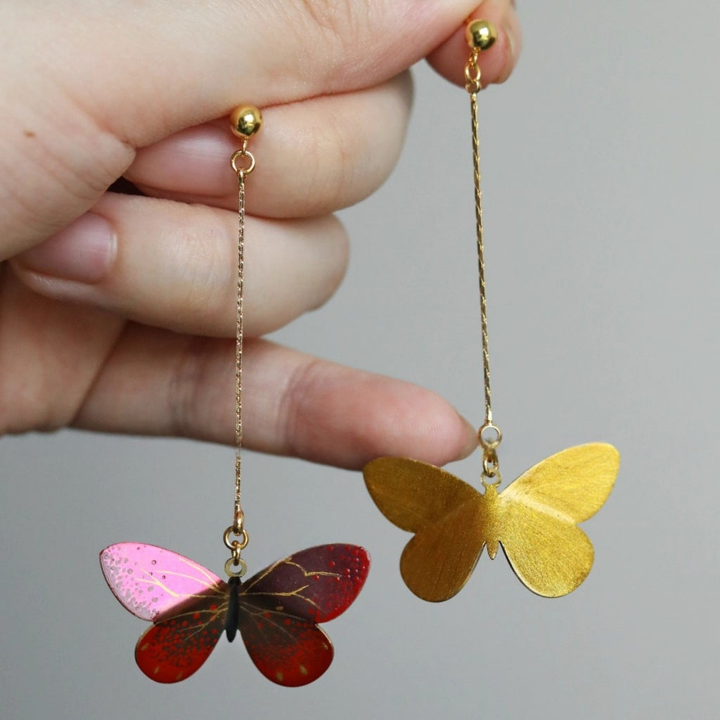 Butterfly-shaped earrings held by a hand against a neutral background