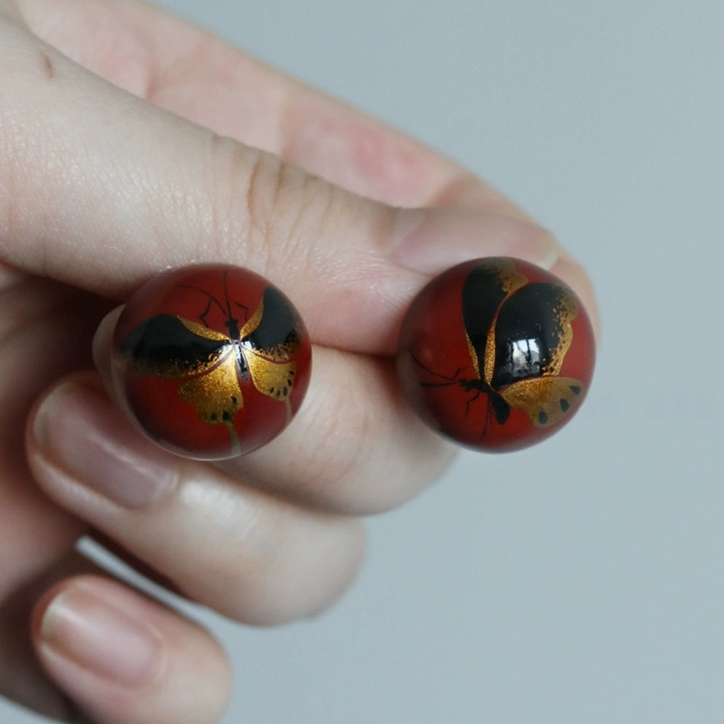 Two red balls with black and gold designs held in a hand against a plain background