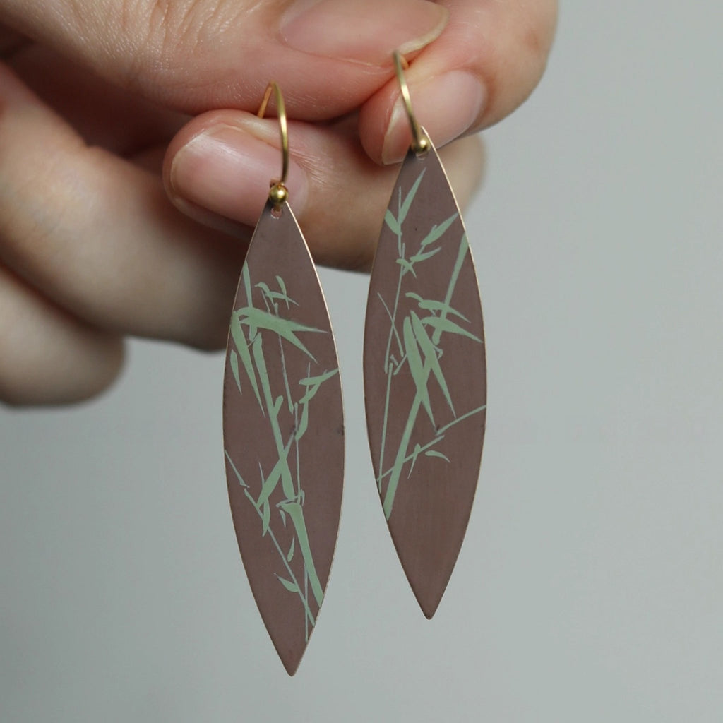 Earrings with leaf-shaped design held by a hand against a neutral background