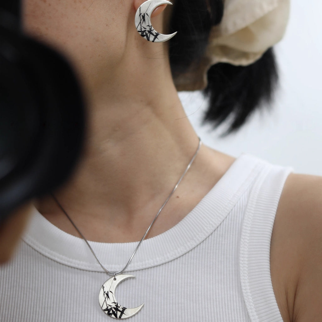 Person wearing a white sleeveless top with a necklace and earrings featuring crescent moon designs.