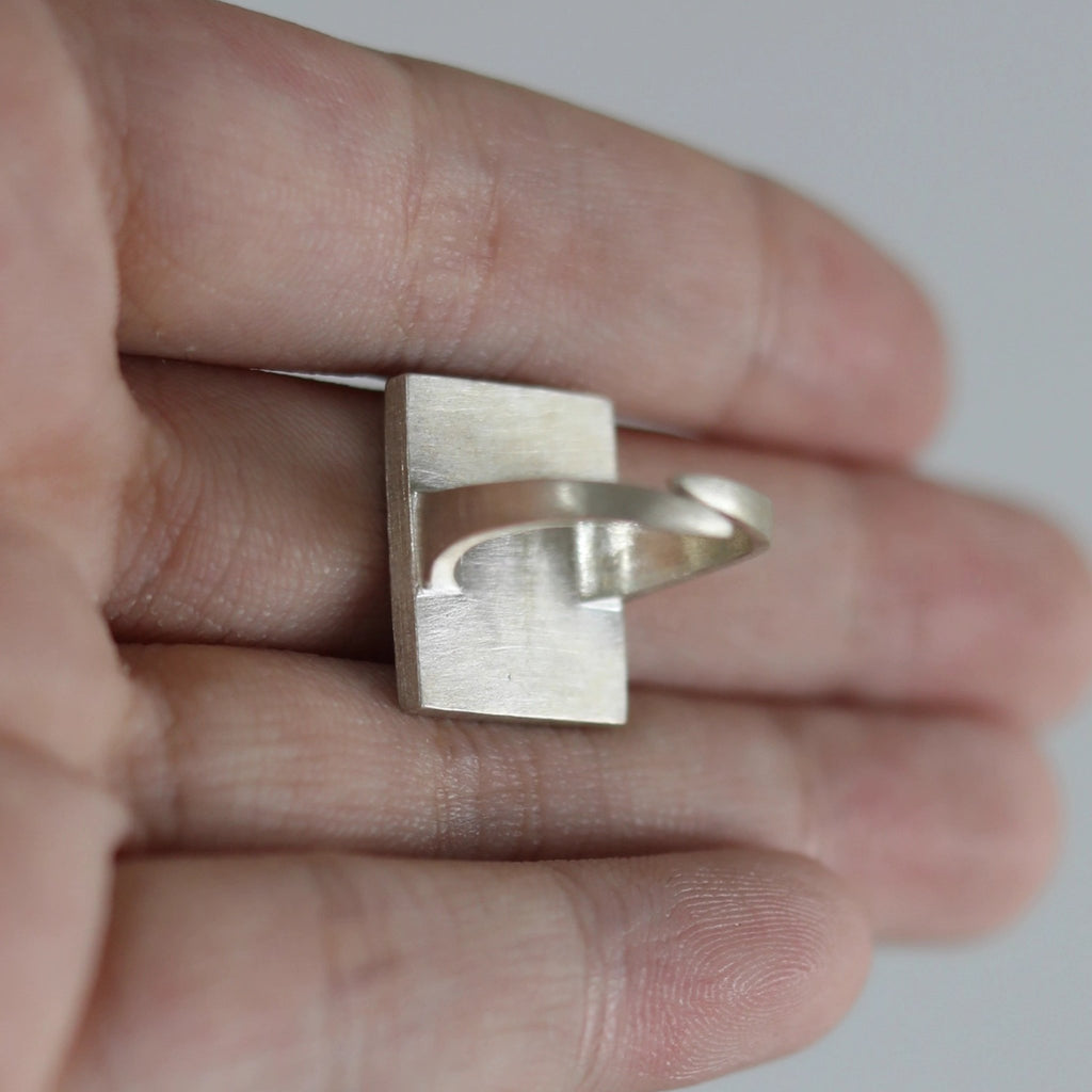 Silver ring held between fingers against a neutral background