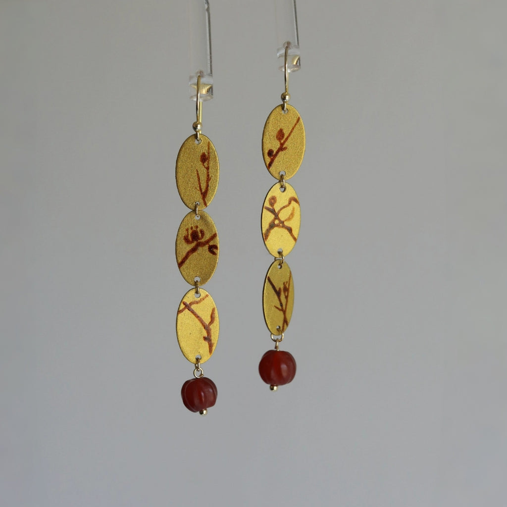Gold and red dangling earrings on a gray background
