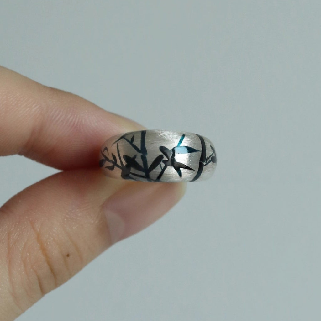 Silver ring with black floral design held between fingers against a plain background