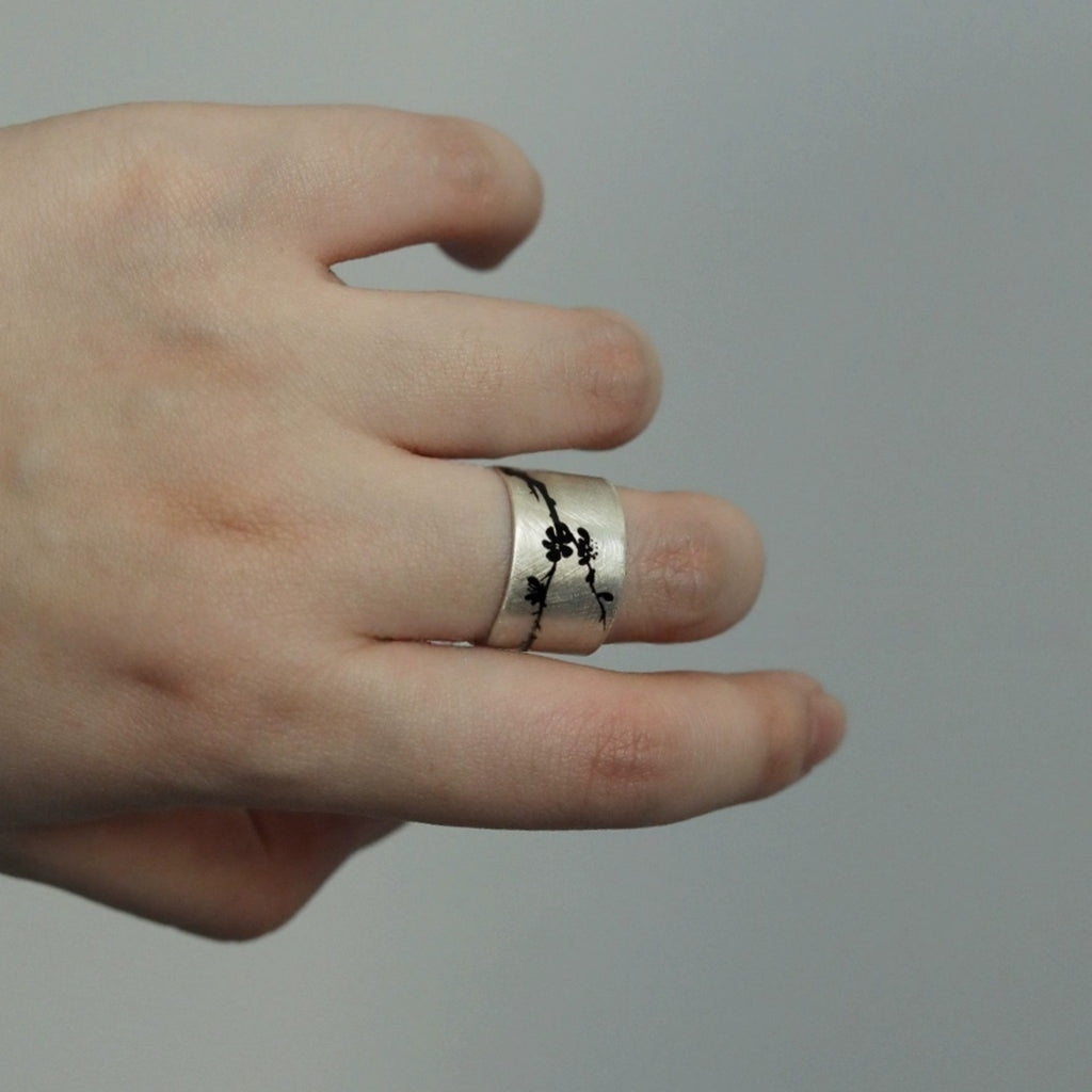Hand wearing a silver ring with black floral design on a gray background