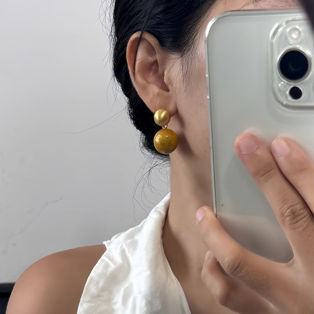 Person wearing gold earrings, holding a phone to their ear with a plain background