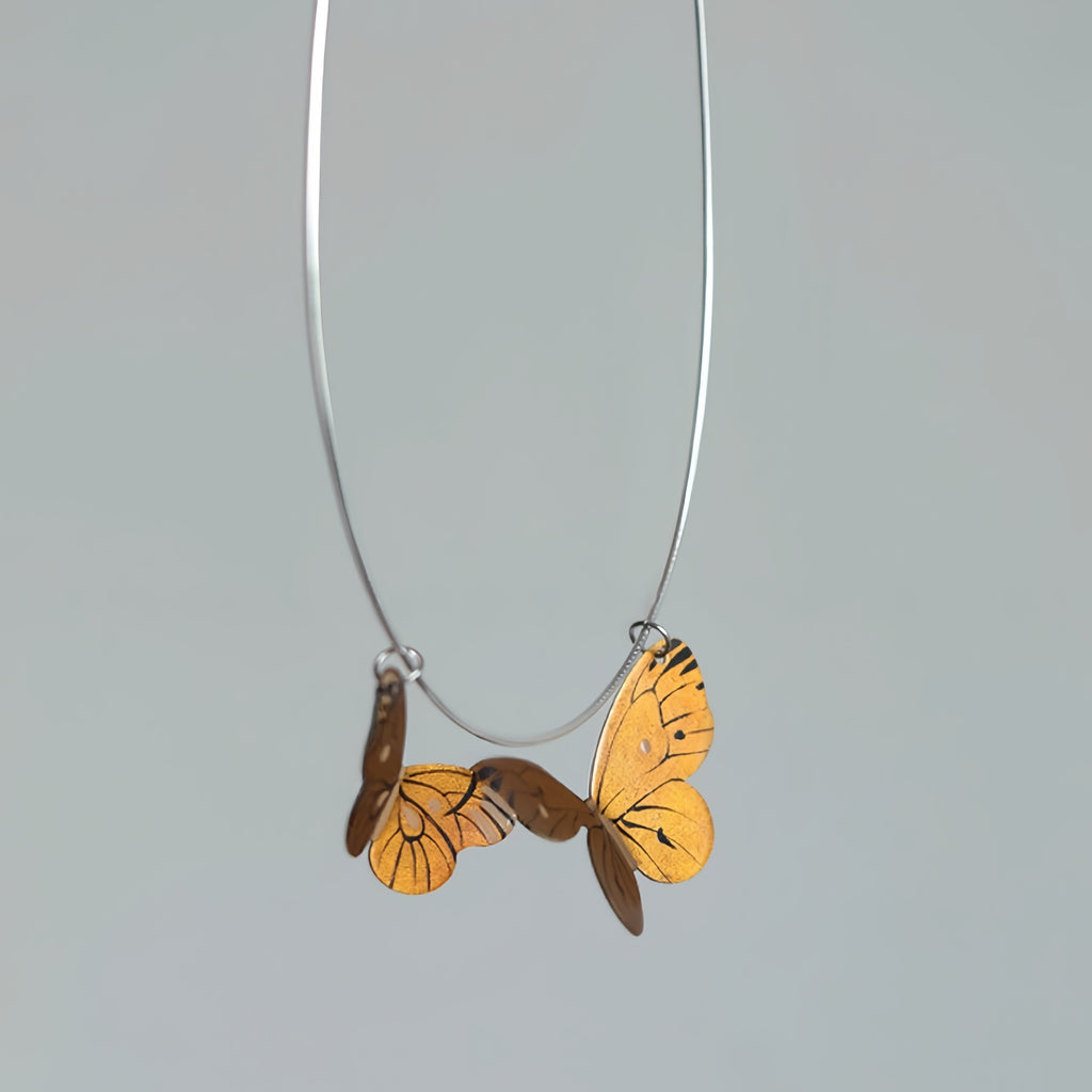 Butterfly-shaped pendant on a silver chain against a gray background
