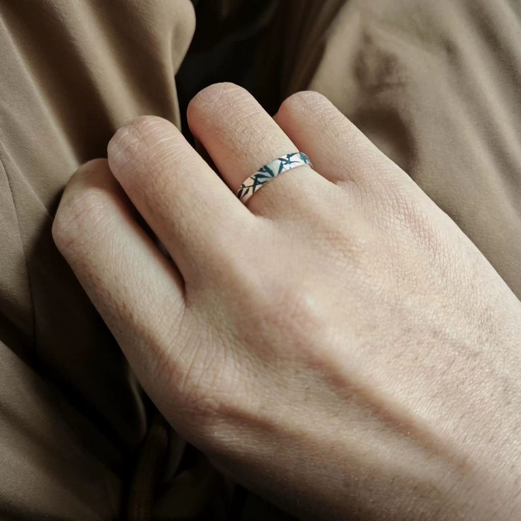 Close-up of a hand wearing a silver ring with a pattern, against a brown fabric background. LacLume HandPainted Lacquer Ring Hand Drawn Bamboo Shadows Aesthetic Vibe