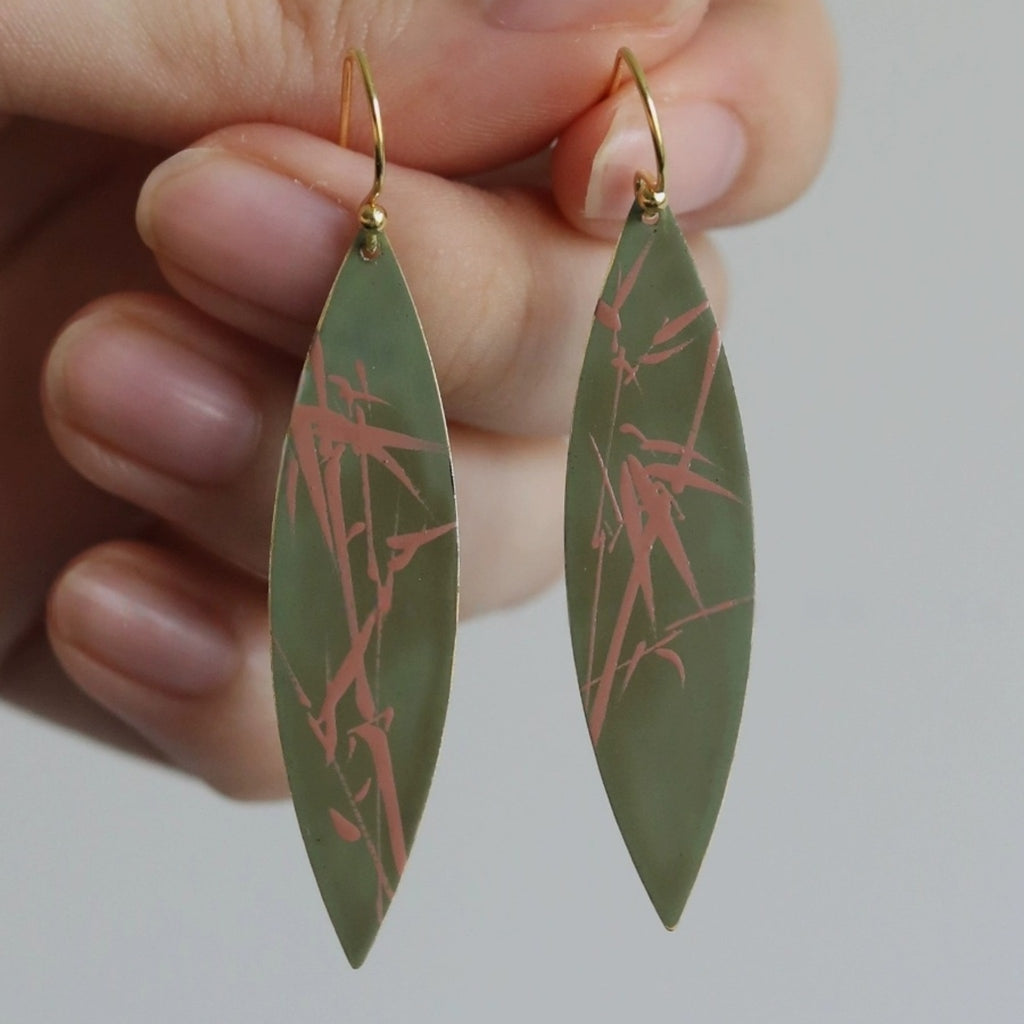 Green earrings with red patterns held by a hand against a neutral background