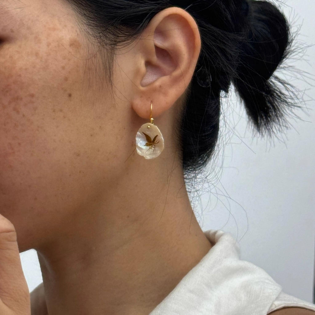 Close-up of a person wearing a clear earring with a butterfly design against a neutral background
