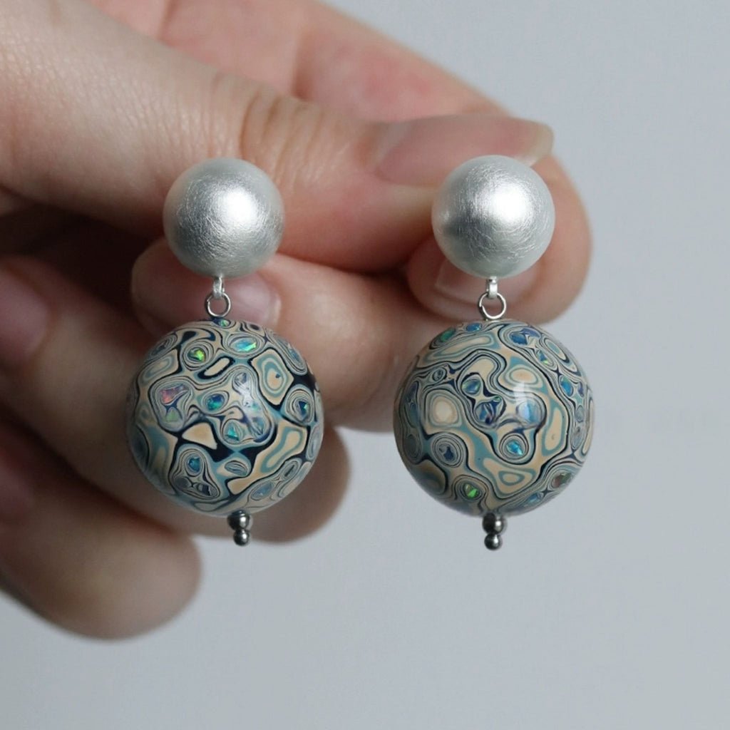Pair of earrings with large spherical beads held between fingers against a white background