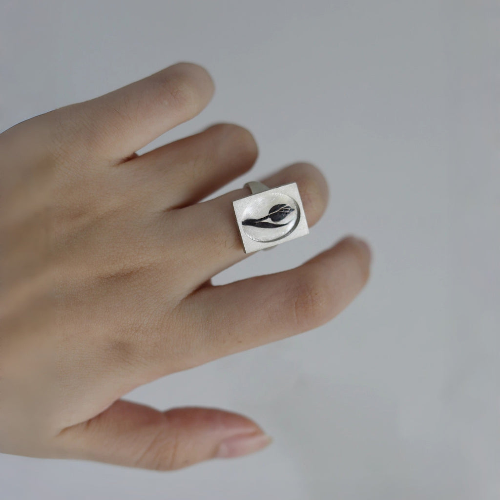 Hand wearing a silver ring with a black design on a light gray background