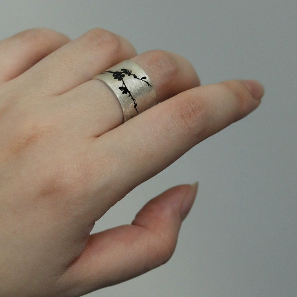 Silver ring with tree design on a finger against a plain background