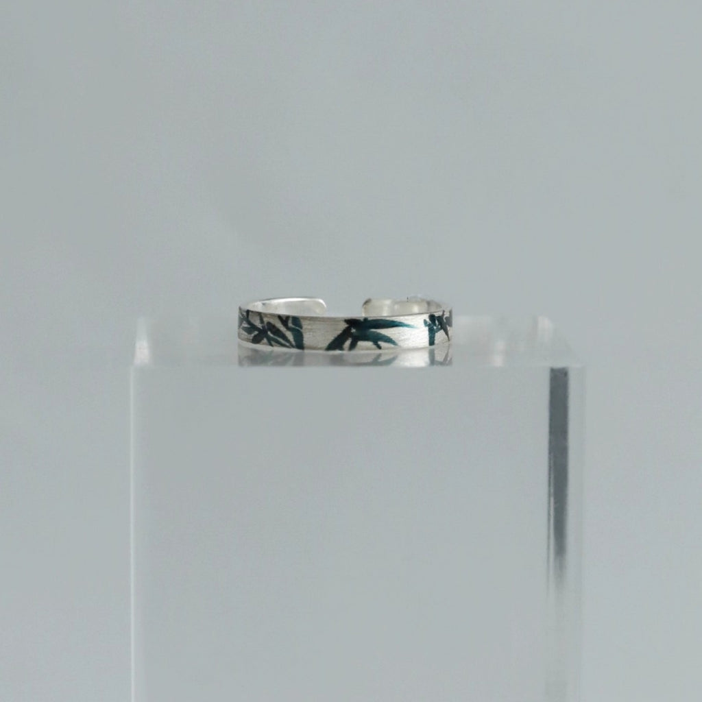 Silver ring with floral design on a clear stand against a light gray background
