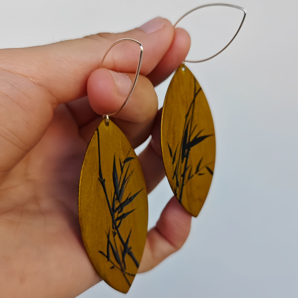Hand holding wooden earrings with leaf design against a white background
