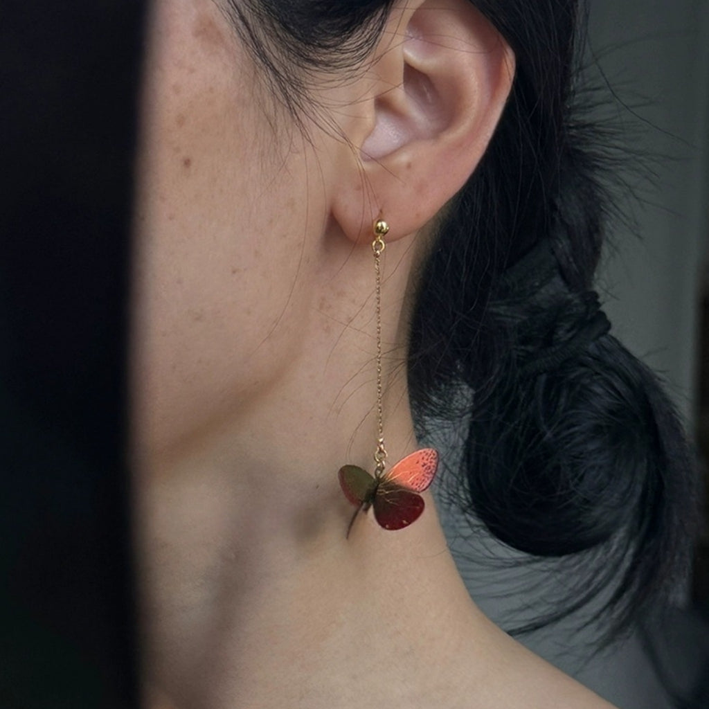 Butterfly-shaped earring worn by a person with dark hair tied back.