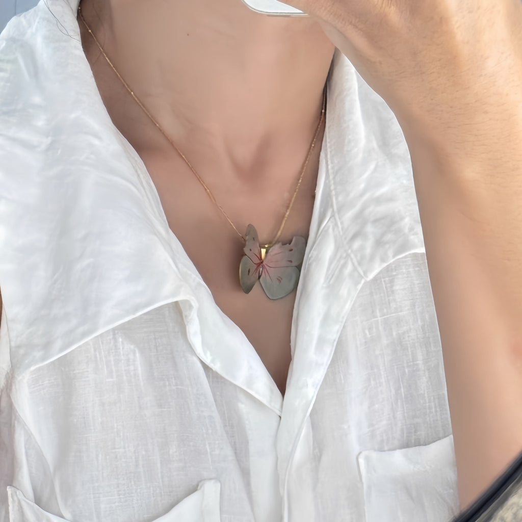 Person wearing a white shirt with a butterfly necklace