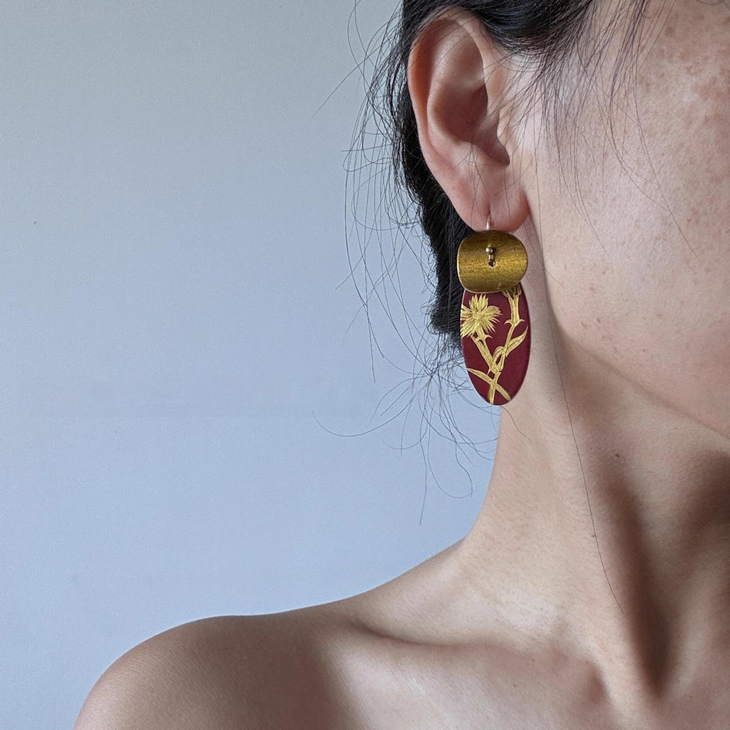 Close-up of a person wearing a gold and red earring against a light blue background