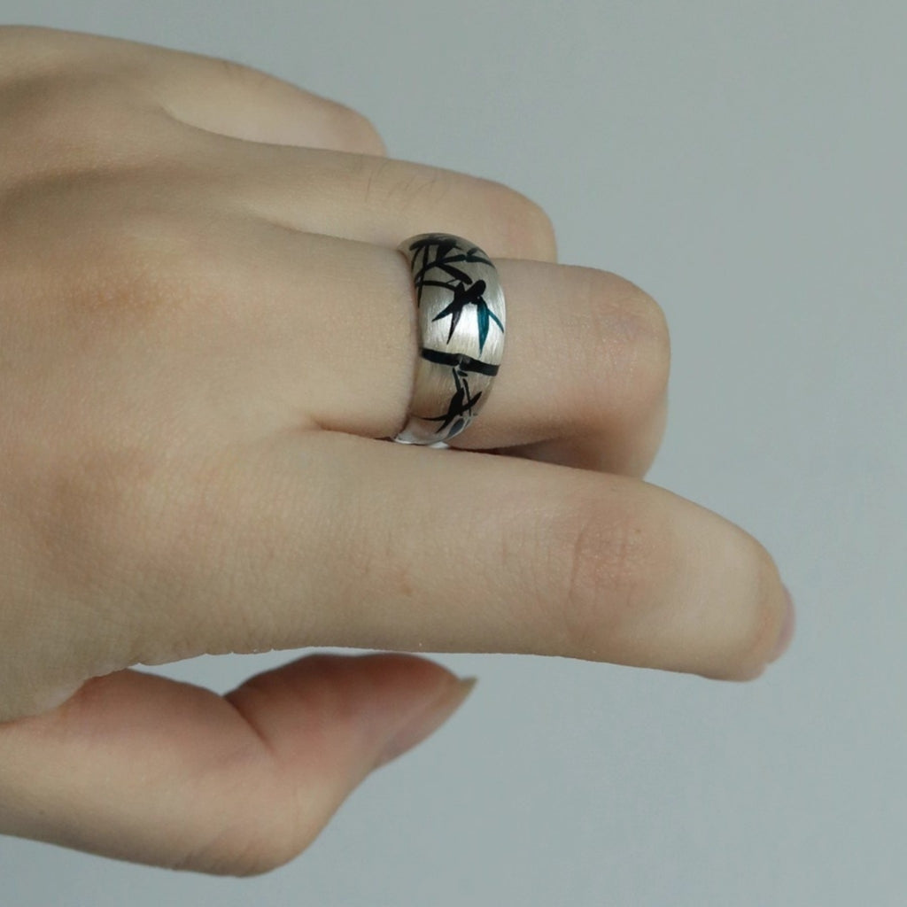 Hand wearing a silver ring with black engraving on a plain background