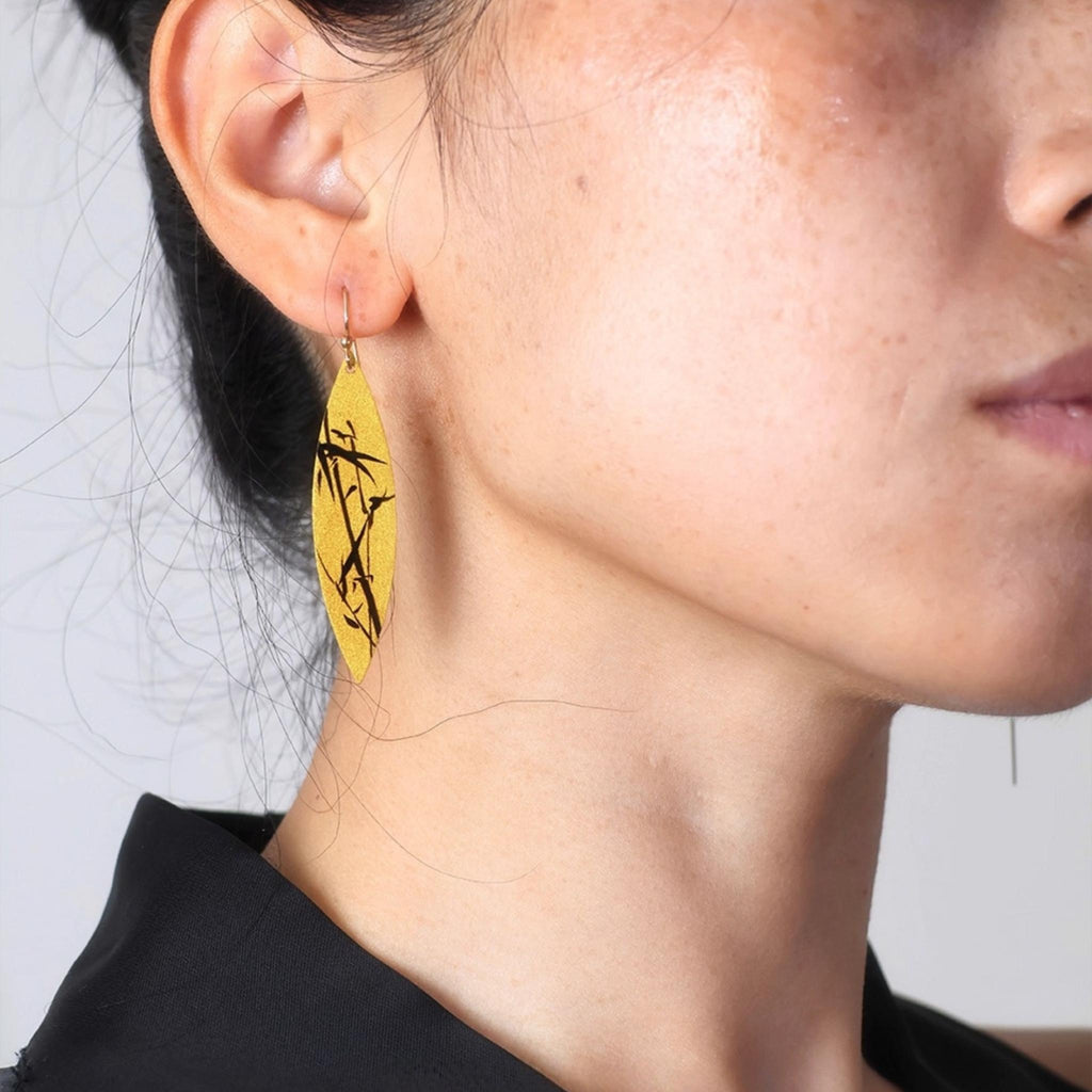 Close-up of a person wearing yellow earrings with black designs.