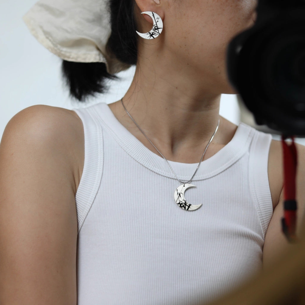 Person wearing a white tank top with a necklace featuring a moon and star pendant.