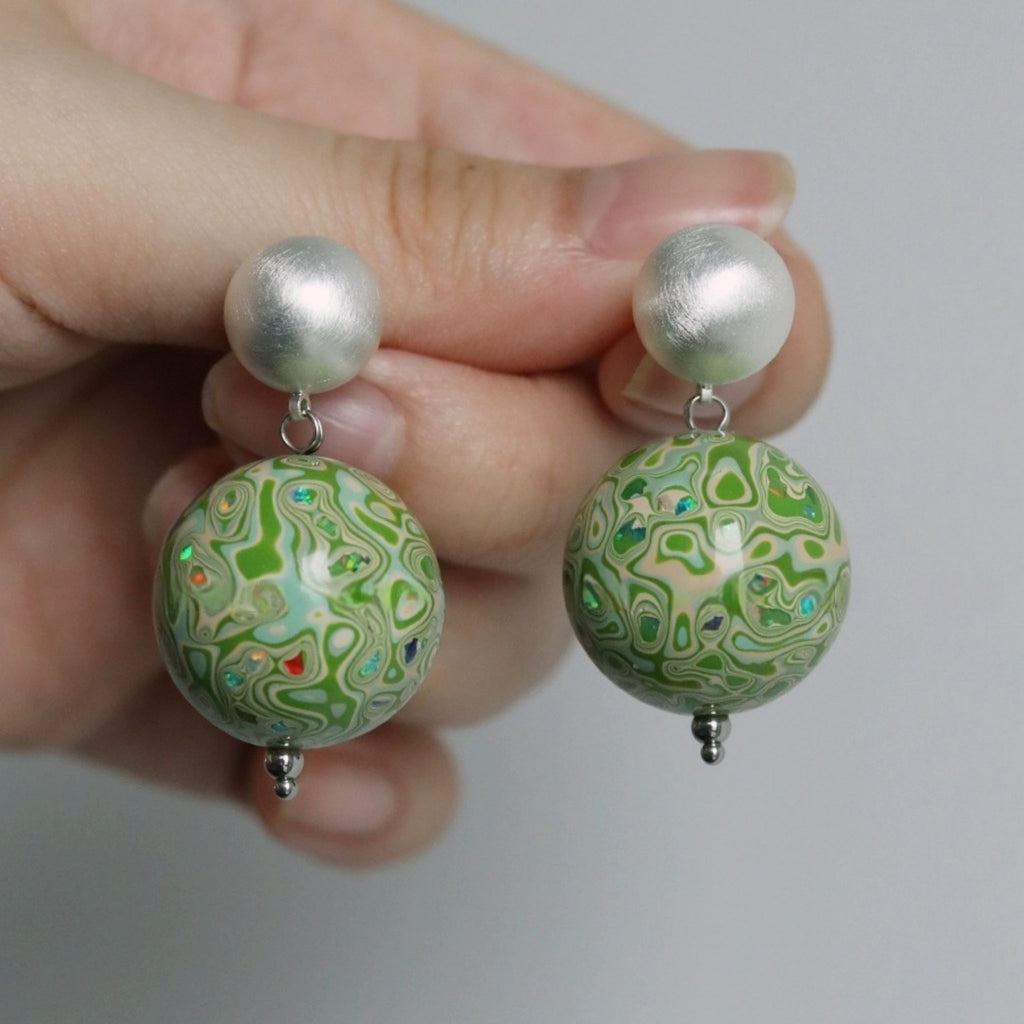 Hand holding a pair of earrings with green marbled design and silver accents.
