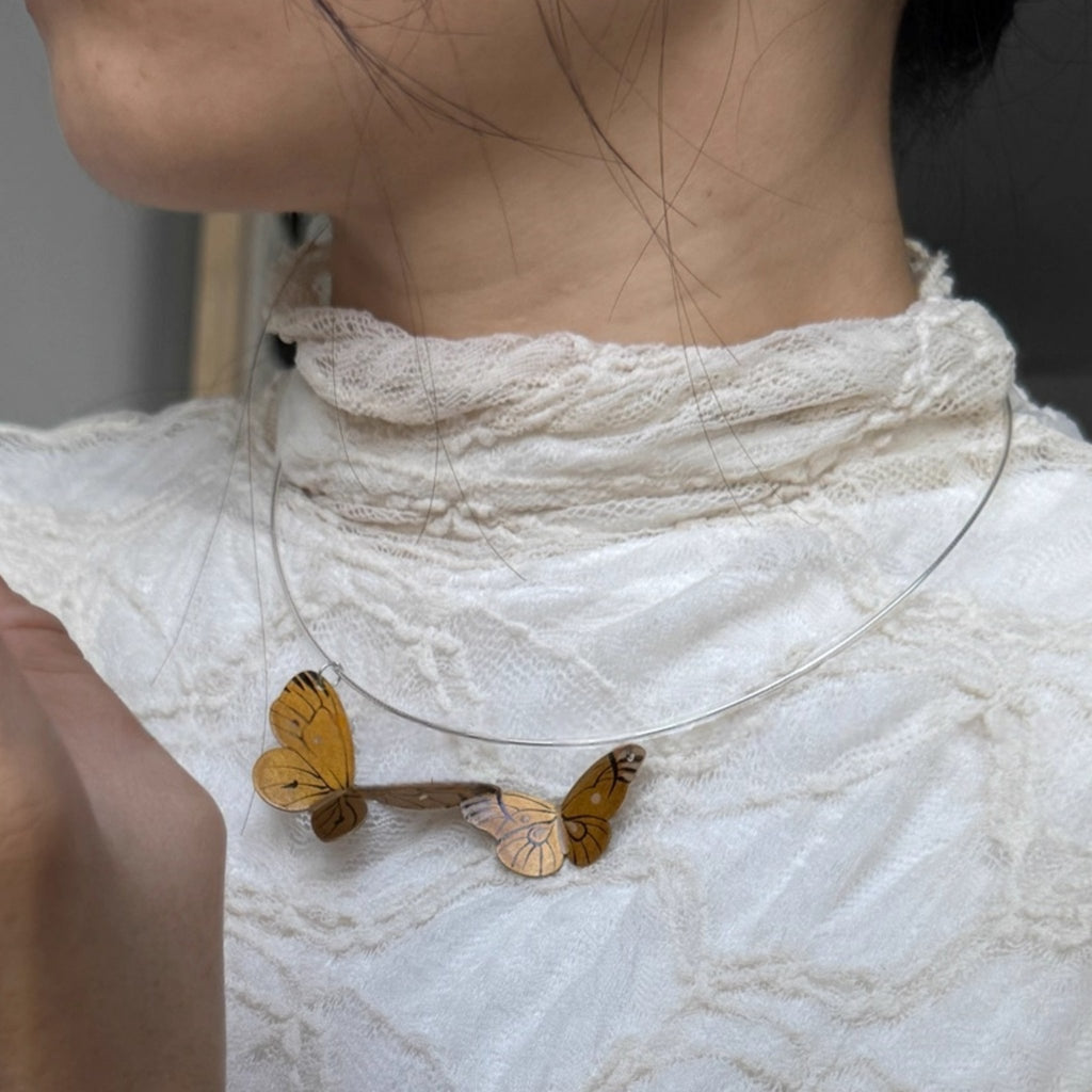 Butterfly-shaped necklace on a person wearing a white lace garment.