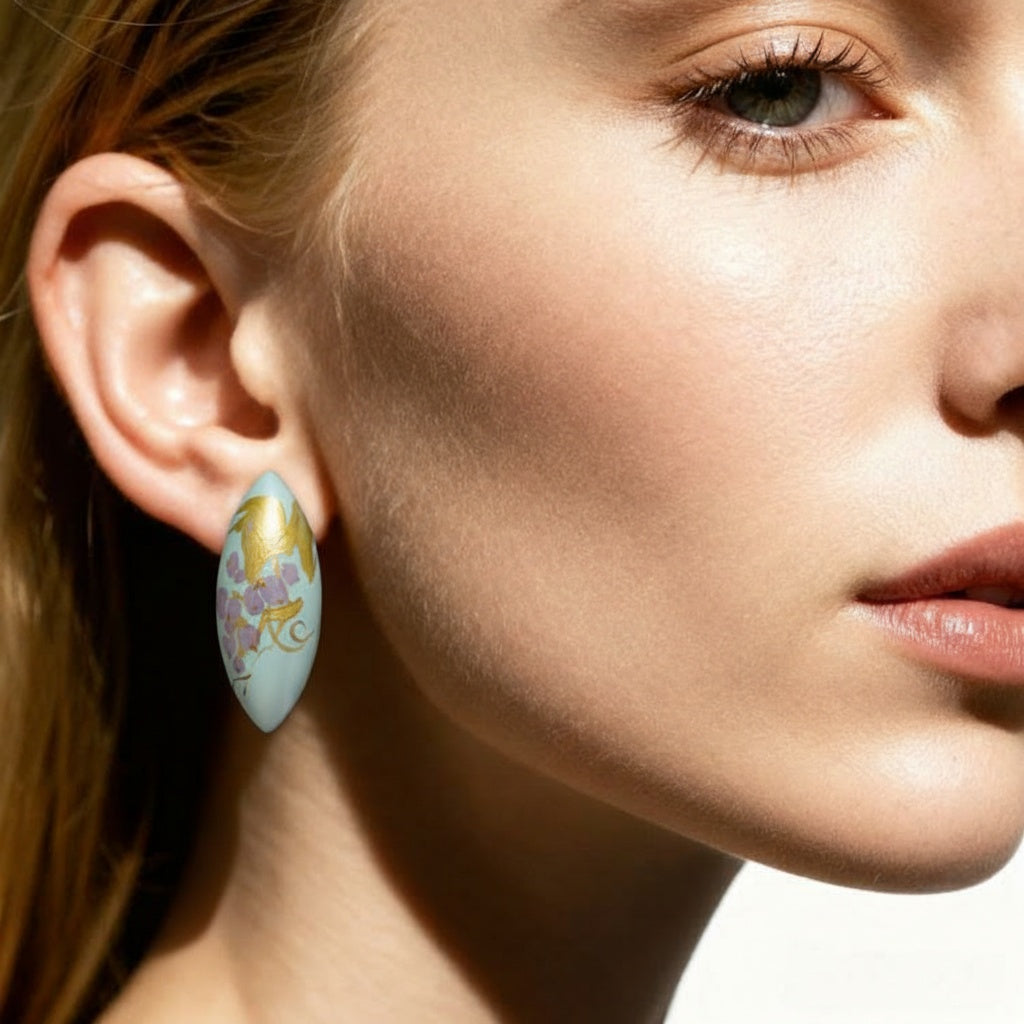 Close-up of a woman wearing a decorative earring with a gold and blue design. LacLume Handcrafted Lacquer Earrings Purple Berry Bubbles Niche Daily Style