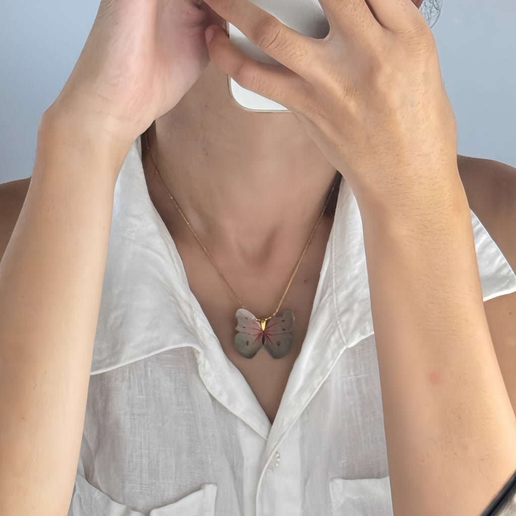 Person wearing a white shirt with a butterfly necklace against a light background