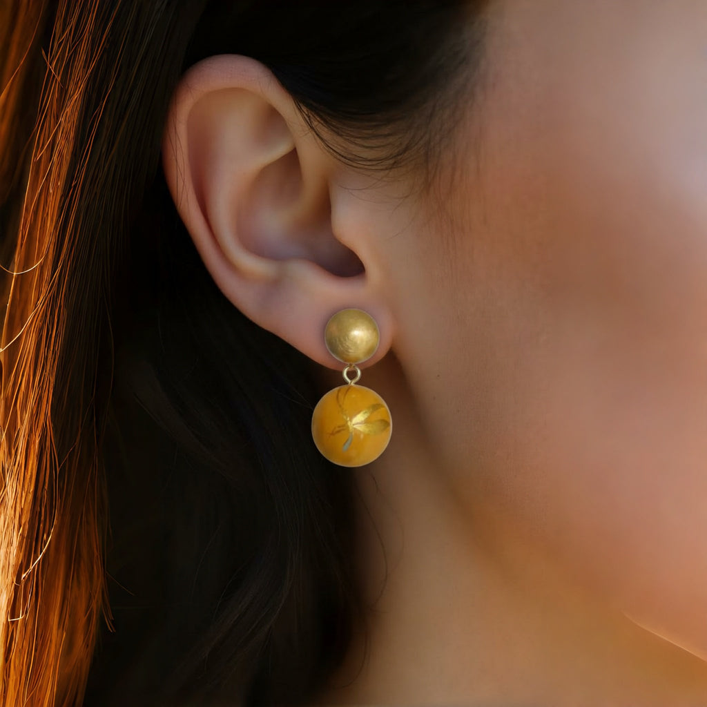 Close-up of an ear wearing a gold and yellow earring with a blurred background