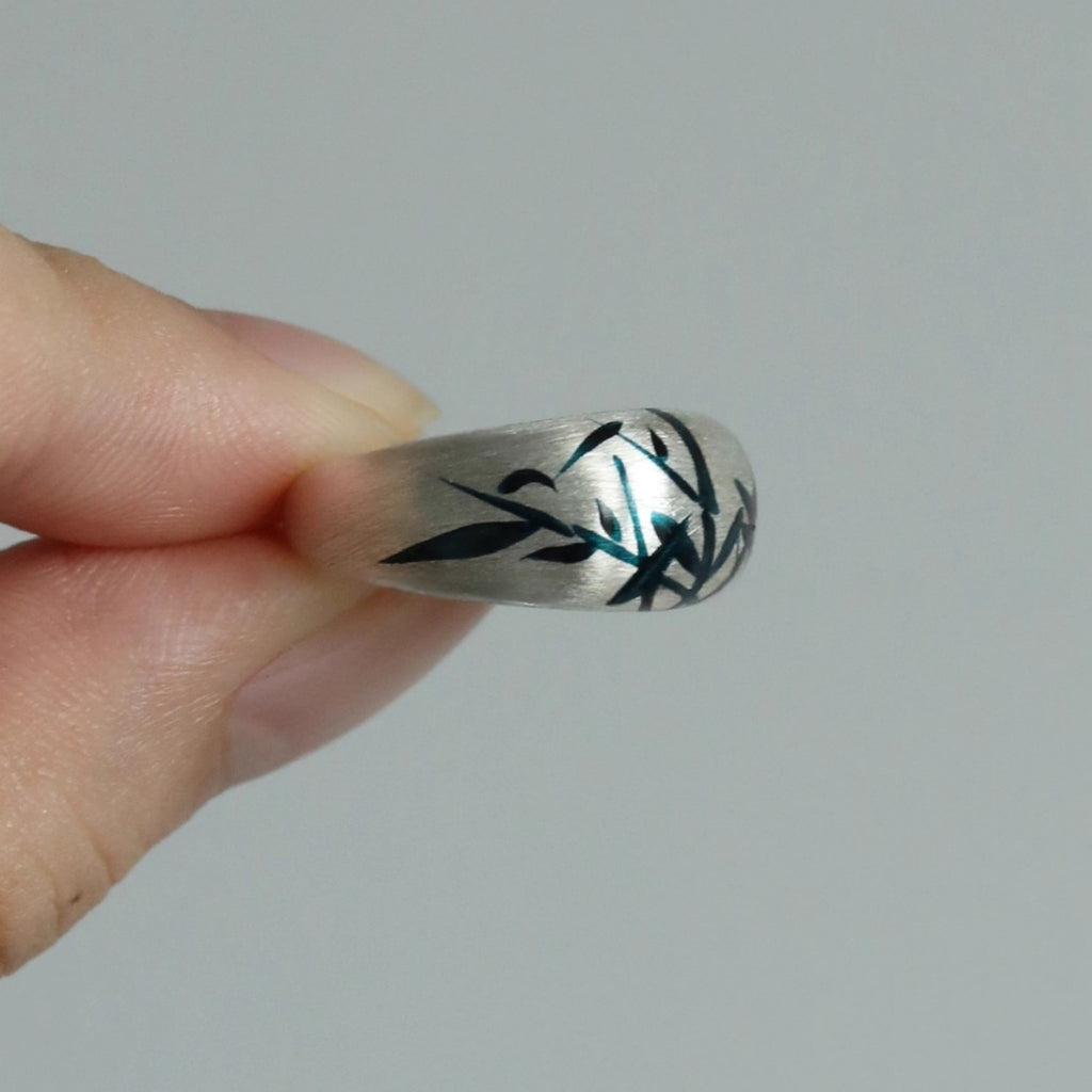 Silver ring with black and green design held by a hand against a gray  LacLume Original Lacquer HandPainted Bamboo Pattern Silver Ringbackground
